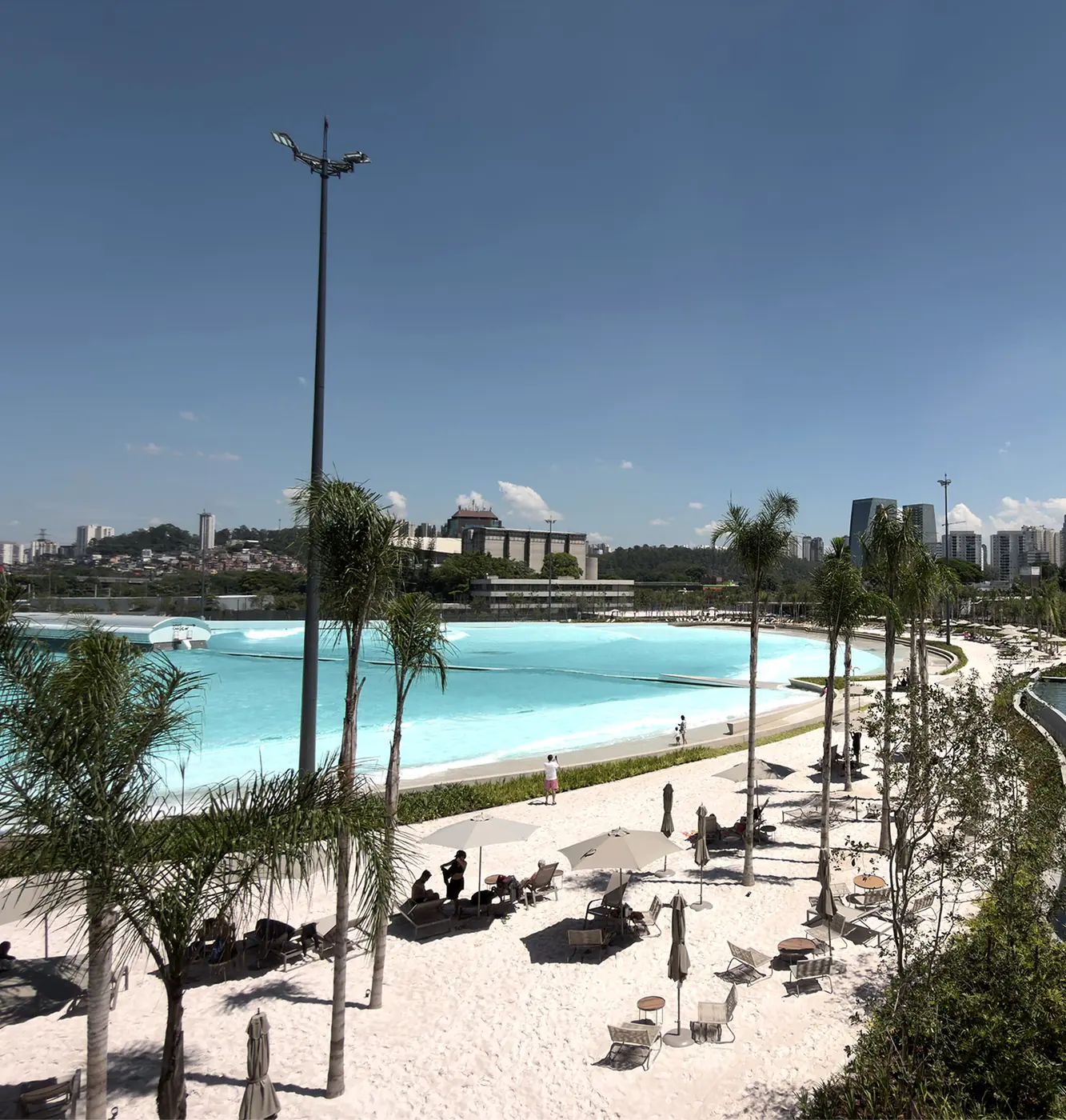 Vista do Beyond The Club, com a piscina de ondas, a praia de areia branca e os prédios de São Paulo ao fundo