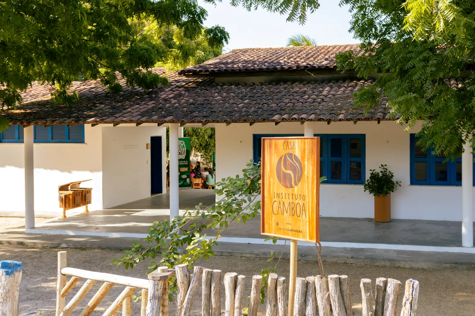 Casa do Instituto Camboa, com telhado de telha e janelas azuis, e uma placa de madeira na entrada