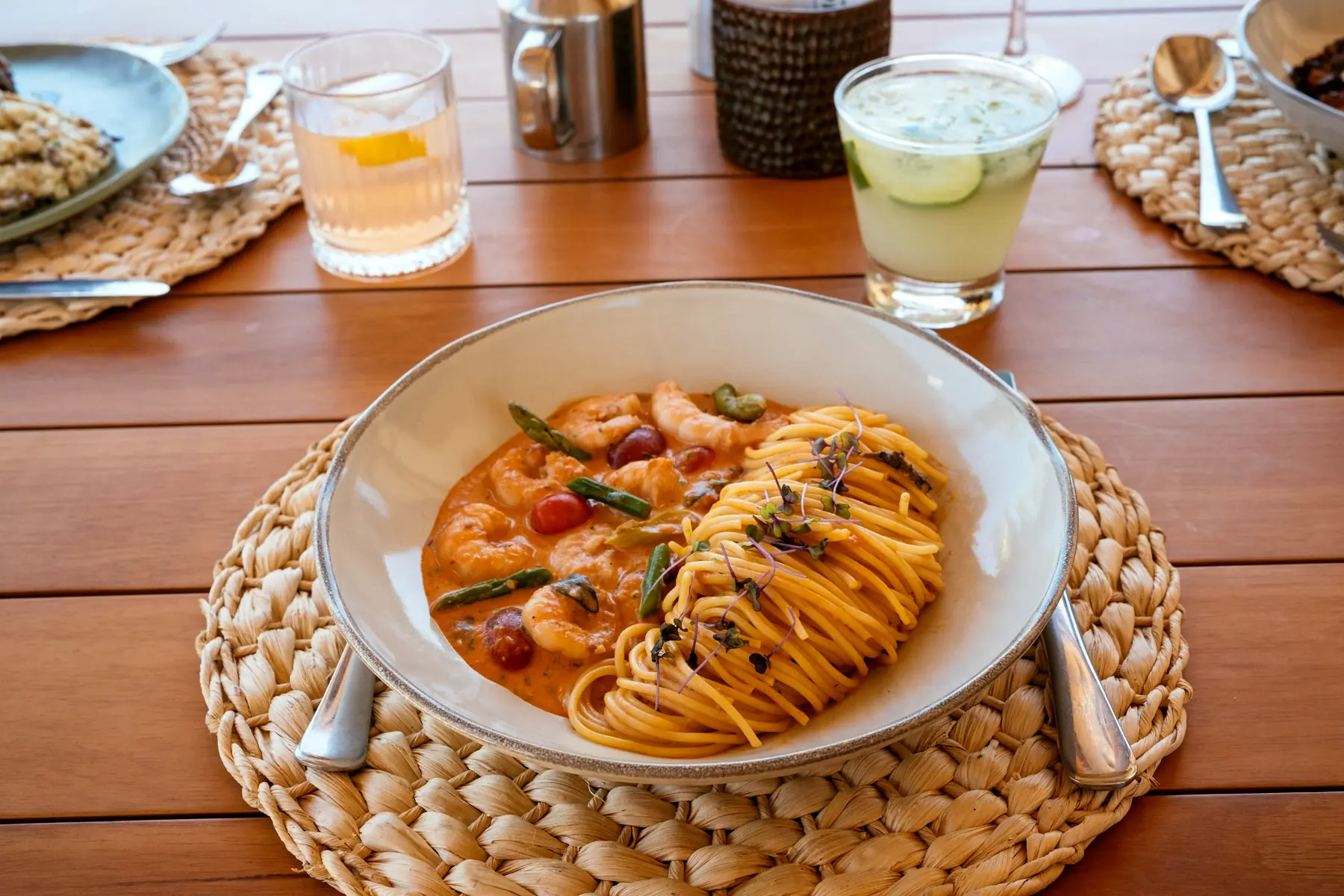 Prato de macarrão com camarão servido em uma mesa de madeira com sousplat de fibra