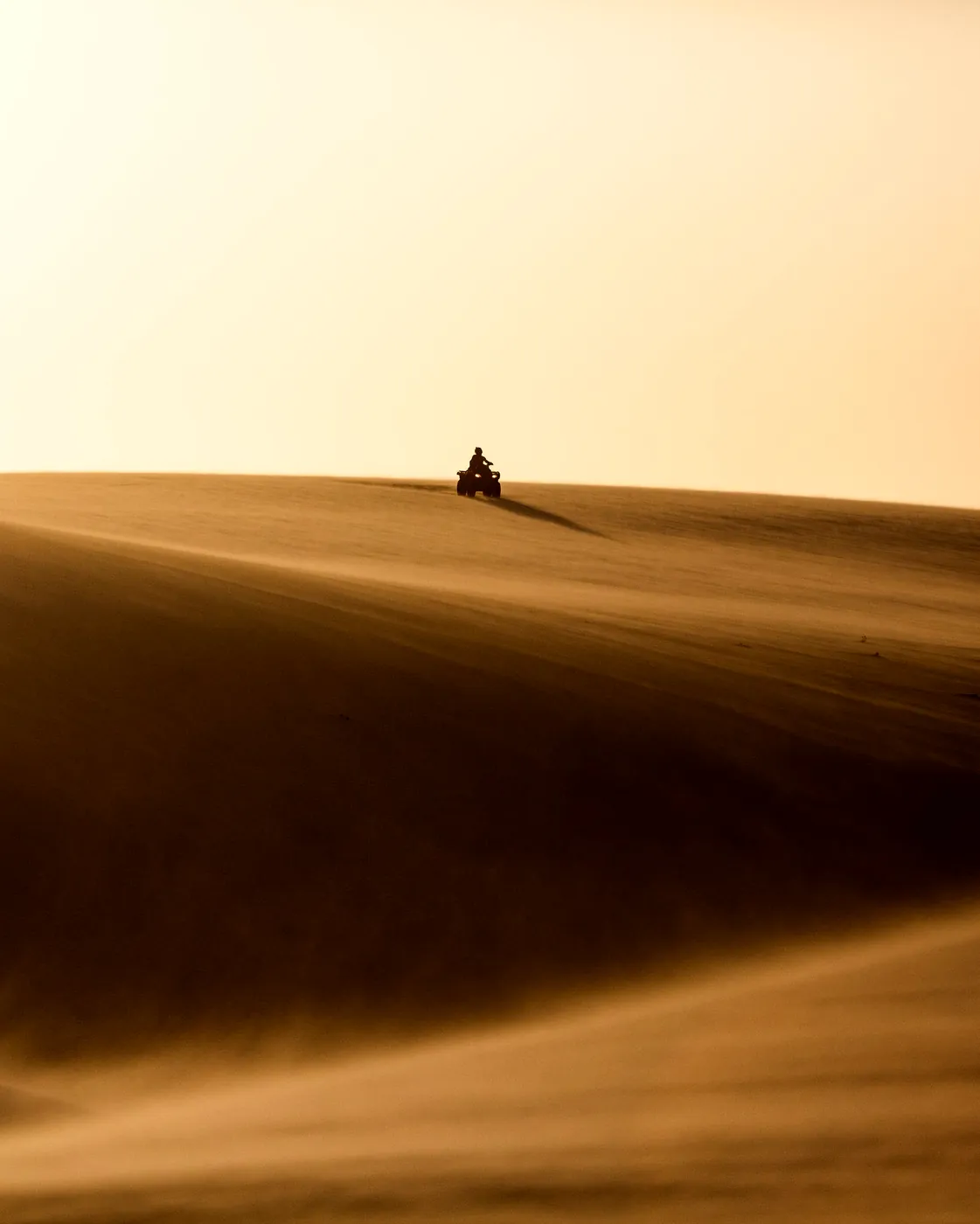 Silhueta de uma pessoa cruzando uma duna ao entardecer